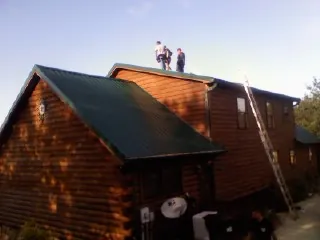 Crew on the ridge of a green metal roof on a two story log home in Rockwood