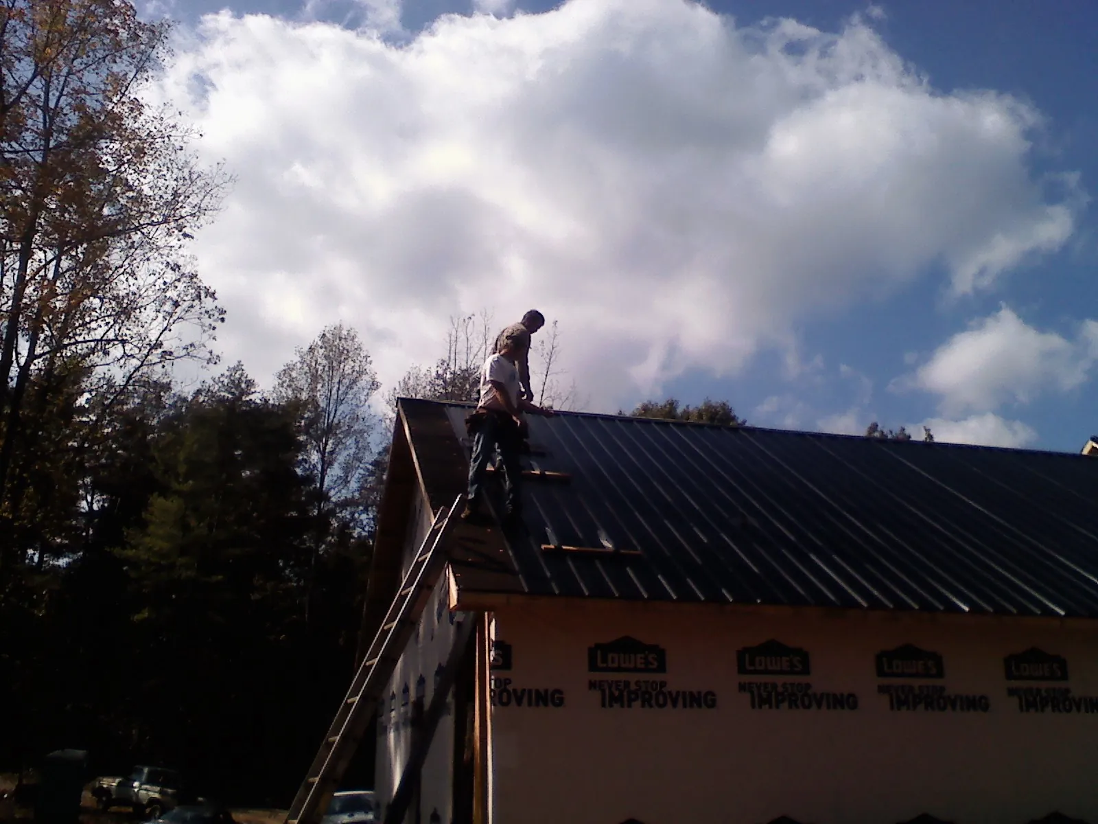 Roofer fastening dark metal panels high against a cloudy sky, from a Roof Inspection job in Rockwood